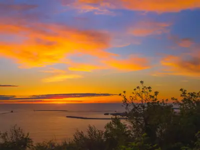 View of sunset from cliff, overlooking the water. The sunset has various deep orange colors. 